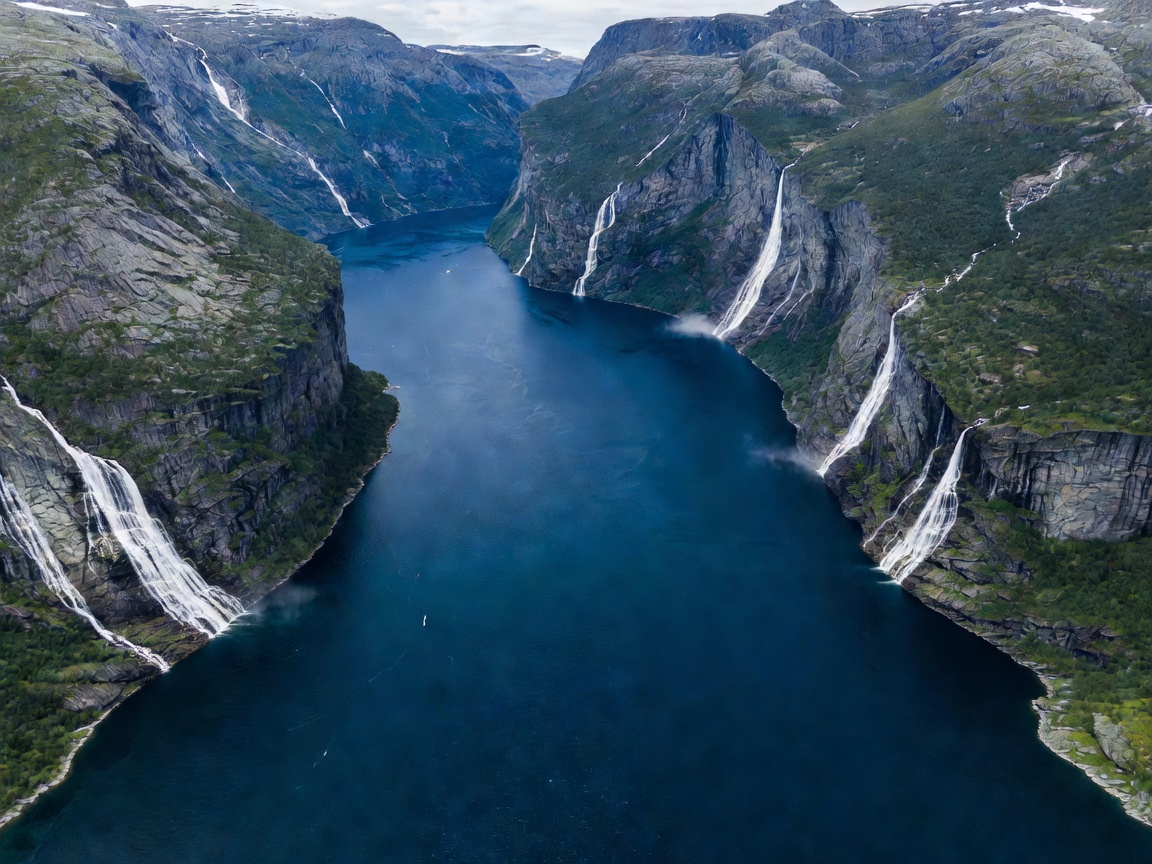 Aerial panorama of the deep blue Geirangerfjord surrounded by sheer waterfalls and cliffs