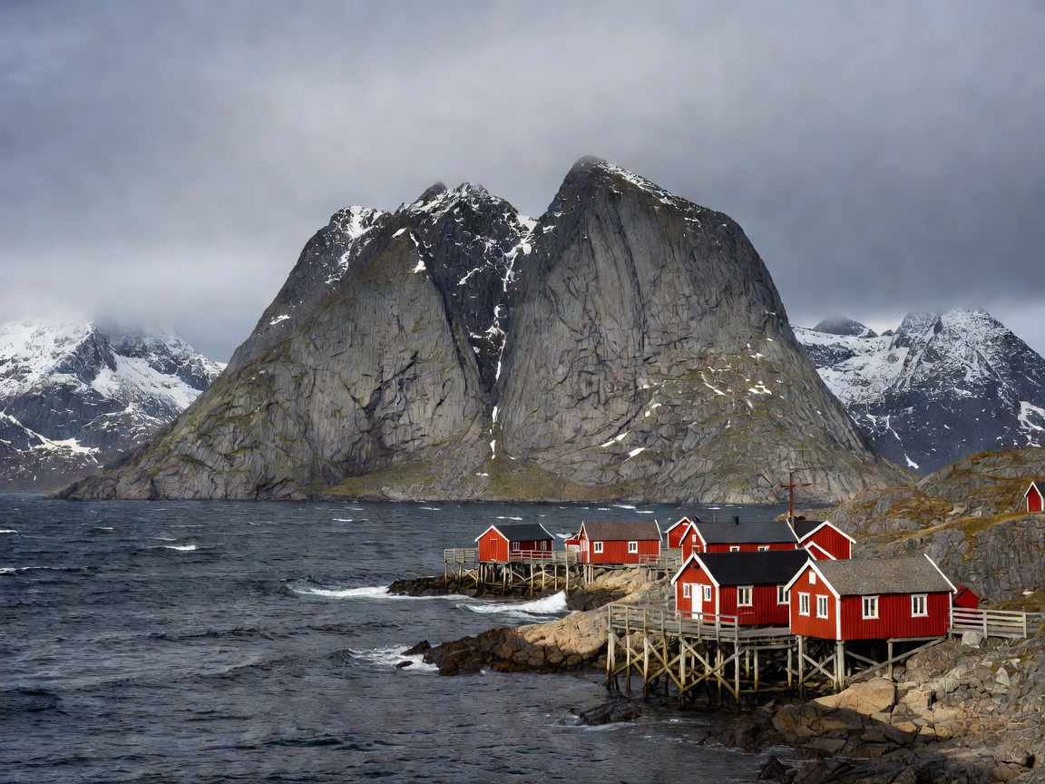 Dramatic granite mountains and traditional red rorbuer cabins in Reine Lofoten Norway